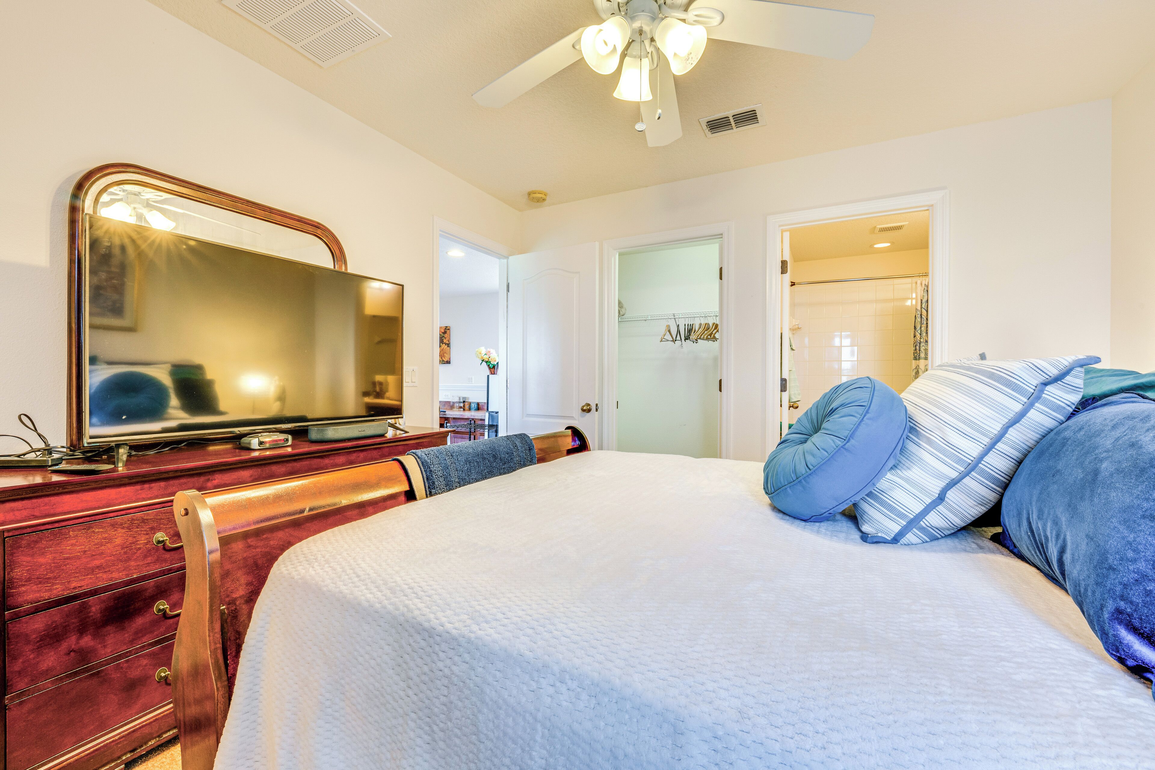 A bedroom with a bed, a dresser, a mirror, and a ceiling fan.
