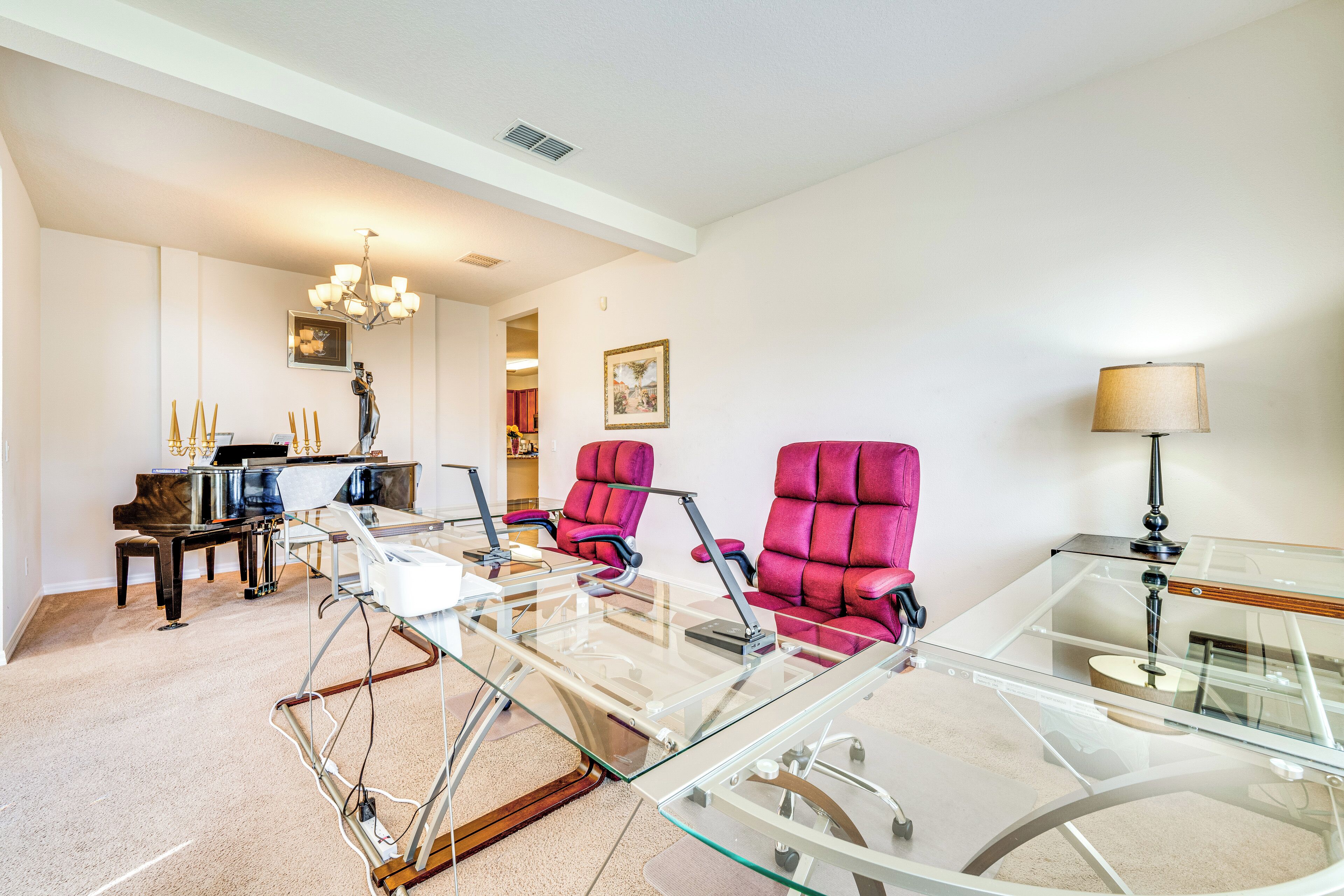 A modern living room with a glass coffee table, two red armchairs, a piano, and a lamp.