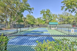 Un court de tennis avec un filet, entouré d’une clôture en treillis métallique et d’arbres.