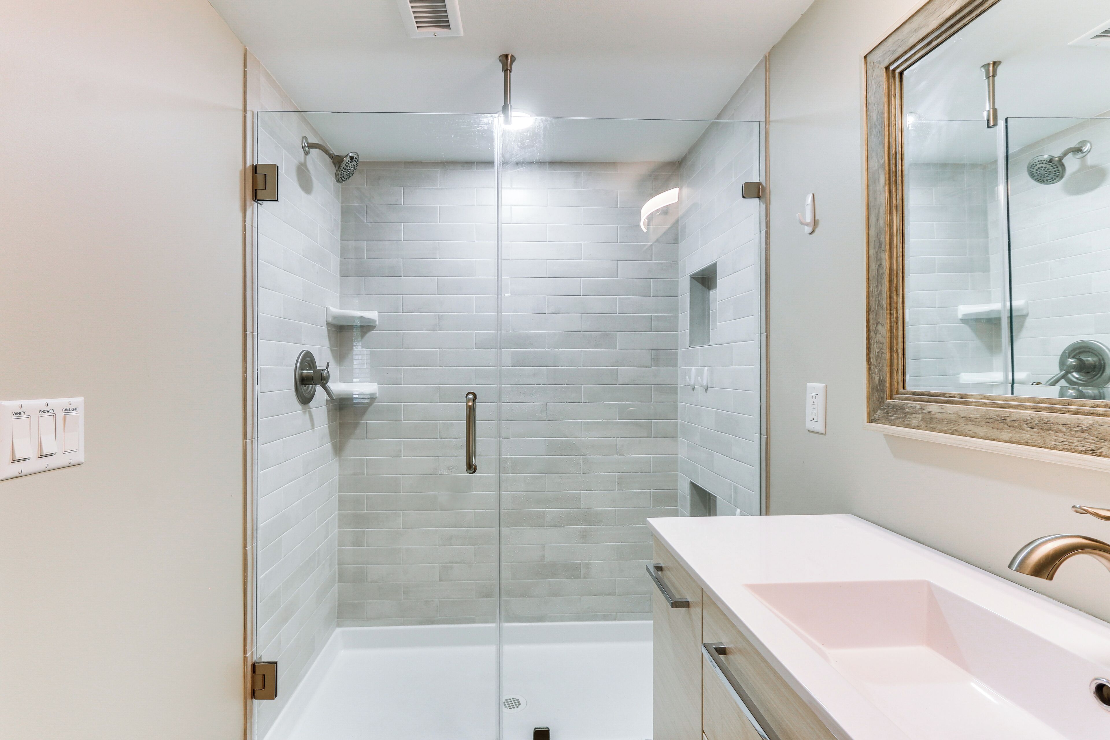 A modern bathroom with a glass-enclosed shower, a white sink, and a mirror with a wooden frame.