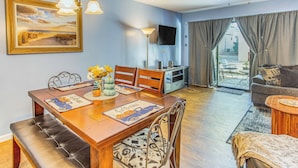 A dining area with a wooden table, chairs, and a bench. There is a television on the wall and a ceiling fan above. - Walk to Ocean: Myrtle Beach Townhome w/ Patio (Myrtle Beach)