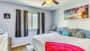 A bedroom with a bed, a ceiling fan, a window with curtains, a painting on the wall, and a nightstand with a lamp. - Walk to Ocean: Myrtle Beach Townhome w/ Patio (Myrtle Beach)