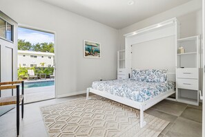 Un dormitorio con cama, un armario blanco, una mesita y vista a una piscina.