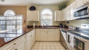 A kitchen with white cabinets, a granite countertop, a stainless steel oven, and a window with blinds.