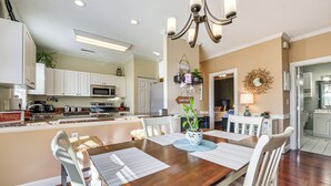 A spacious dining area with a wooden table, white chairs, and a chandelier.