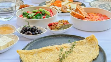 Ein Tisch ist reichhaltig mit verschiedenen Speisen gedeckt, darunter ein großes Omelett, Oliven, Käse und Brot.