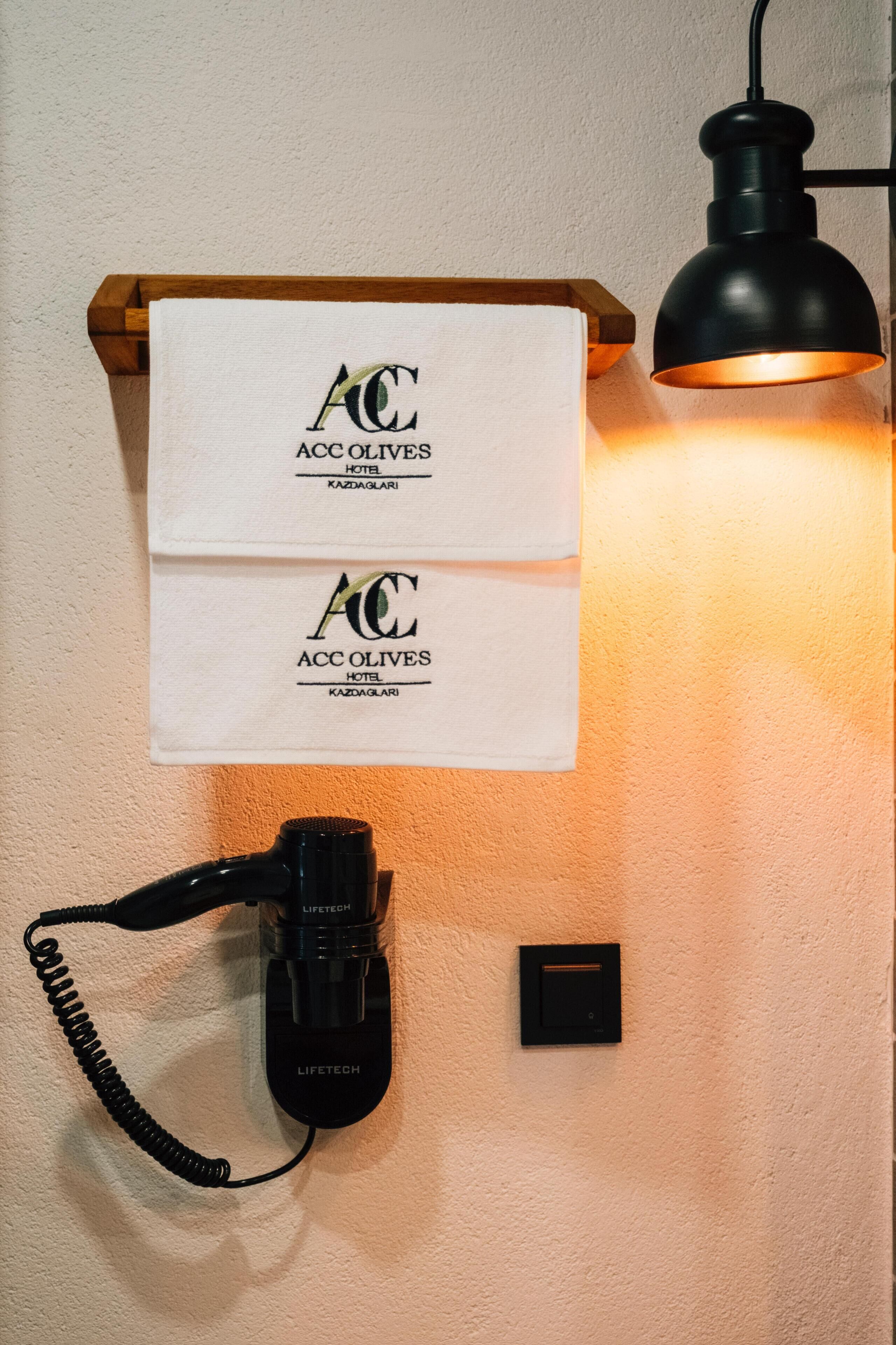 Un teléfono de pared, una lámpara y dos toallas con el logotipo del Hotel ACC Olives.