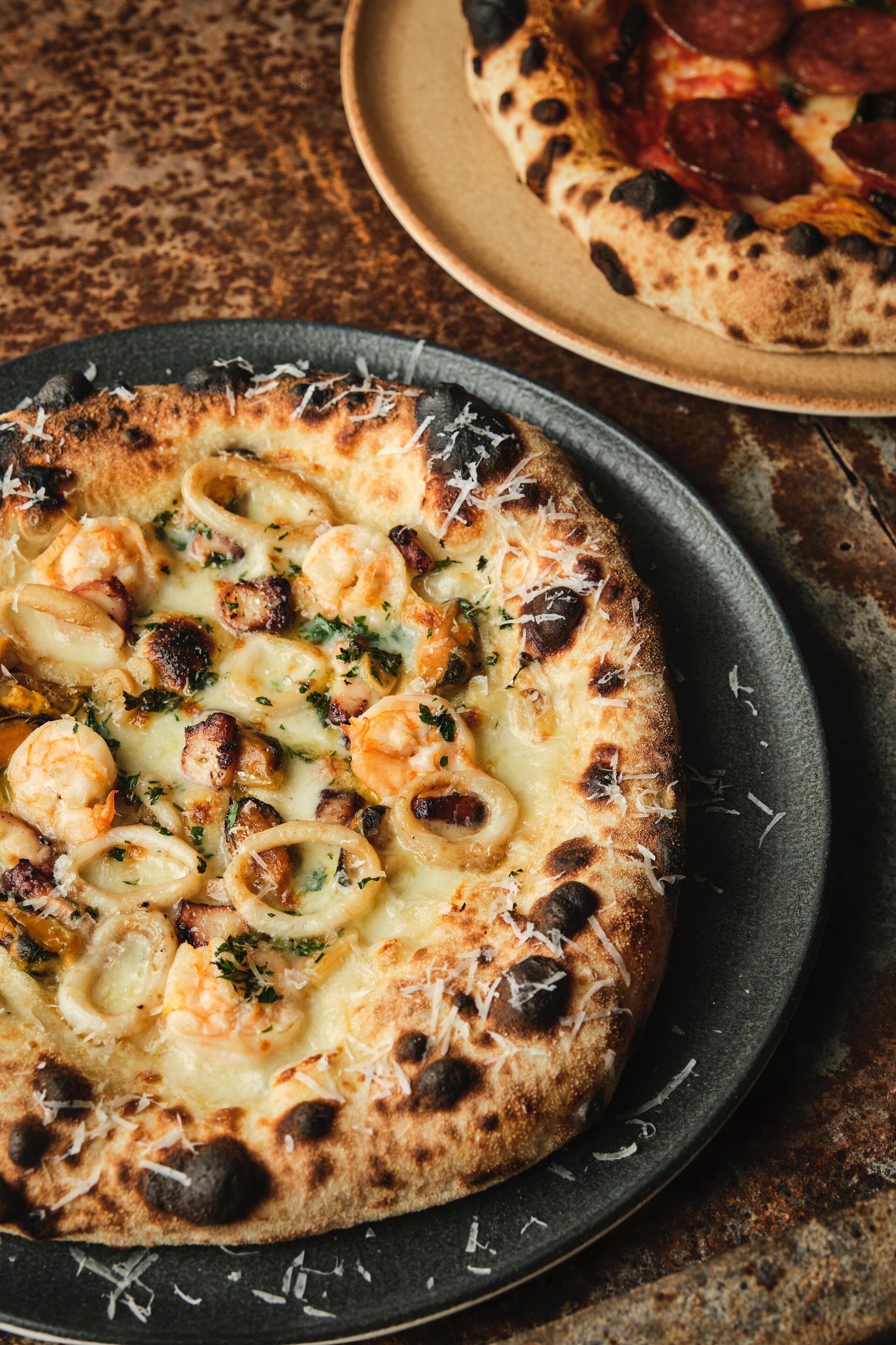 A pizza with shrimp and cheese on a dark plate.