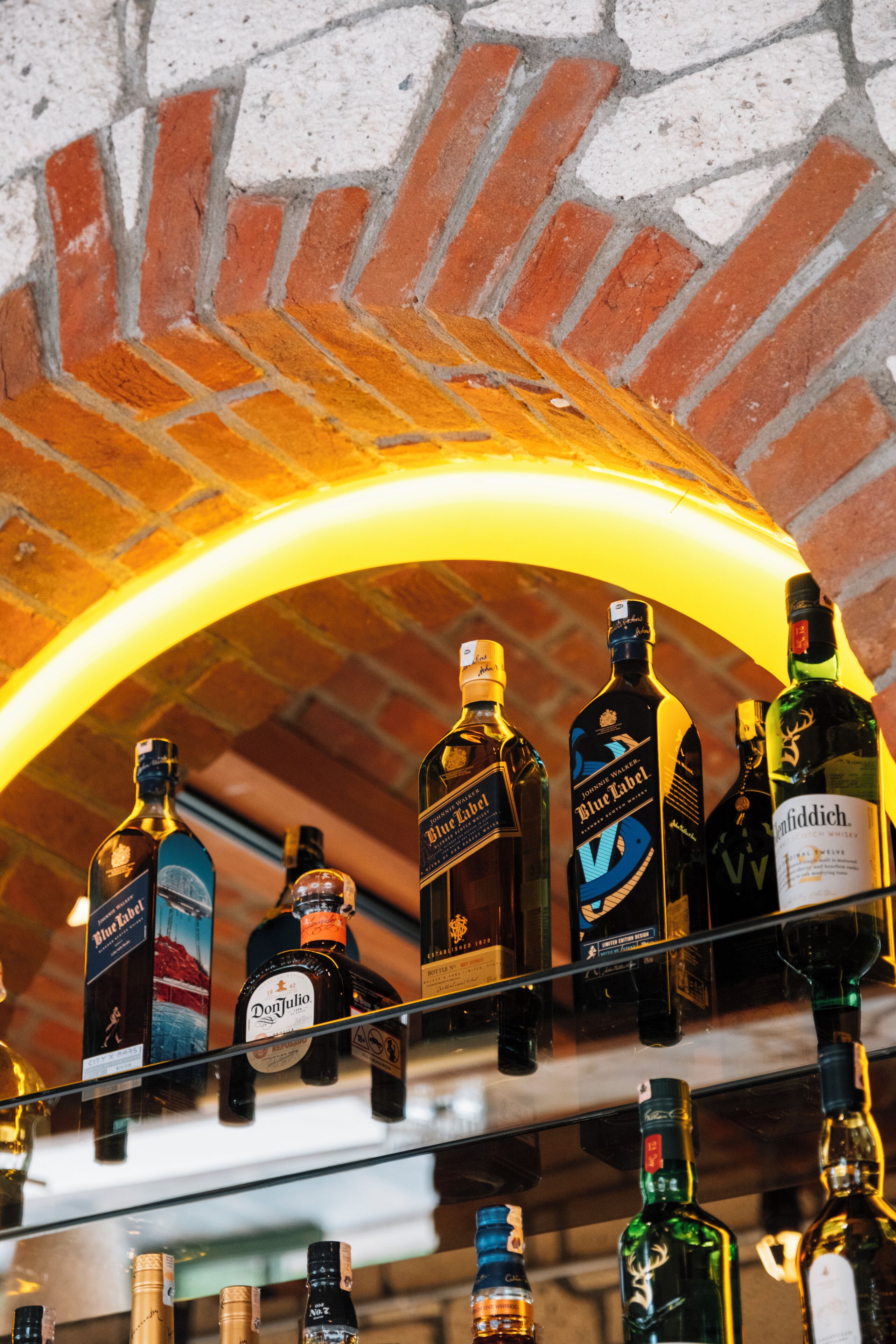Variedad de botellas de licor exhibidas en estantes bajo un arco de ladrillo.