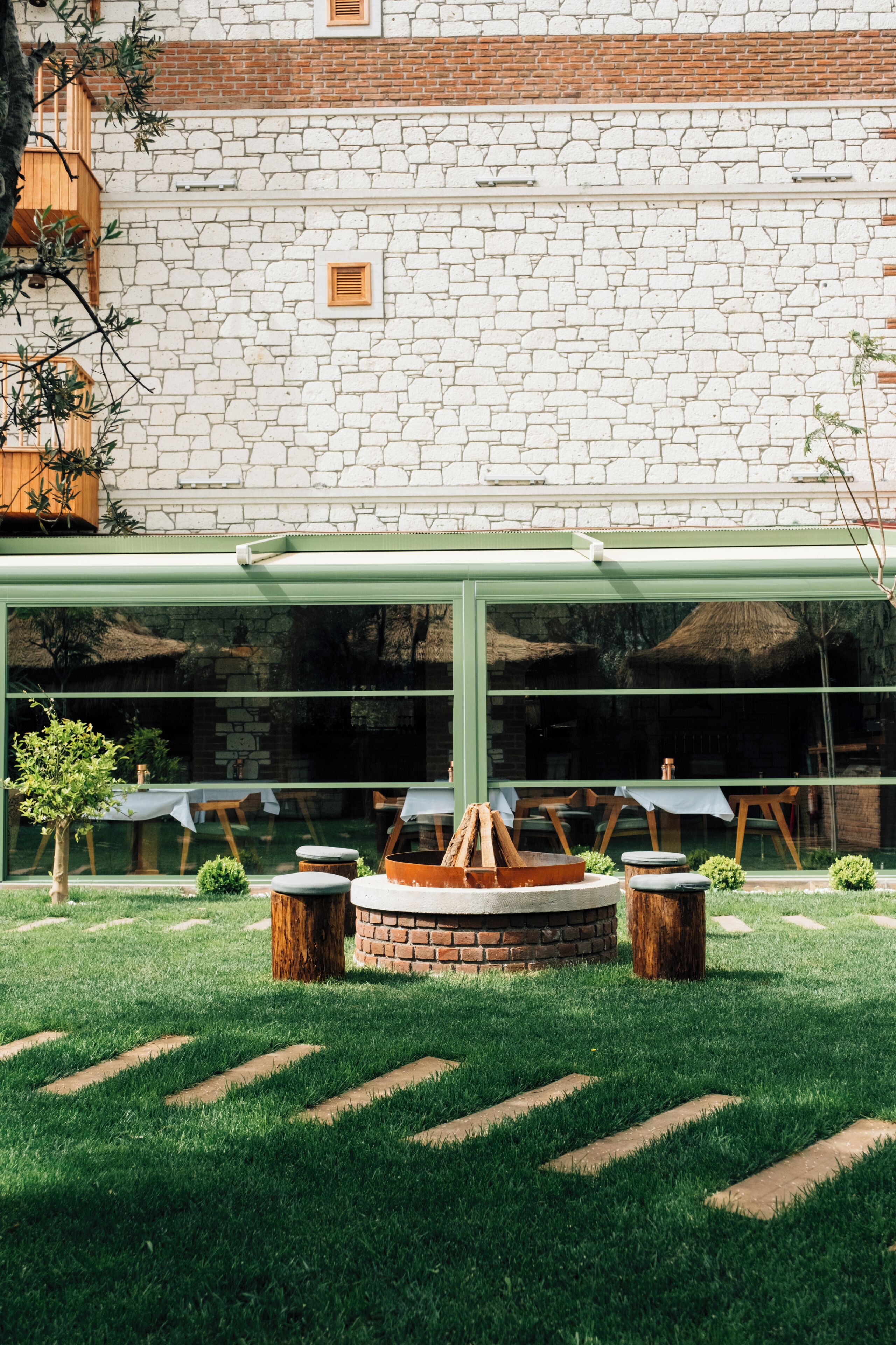 Un mur de briques avec un motif en pierre blanche, une pergola verte et un espace de détente circulaire avec des tabourets.