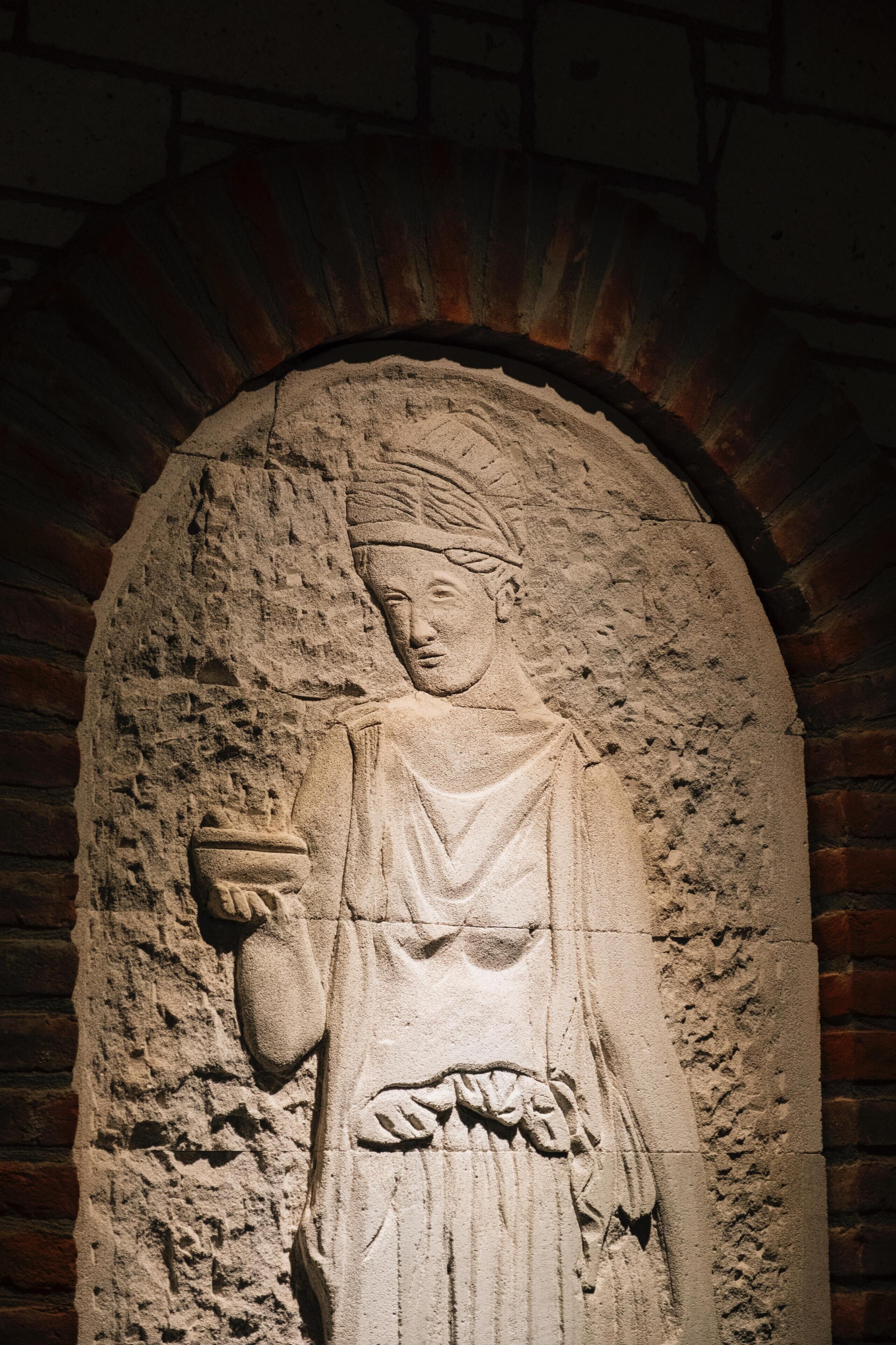 A stone relief sculpture of a figure with a draped garment, set within a brick archway.