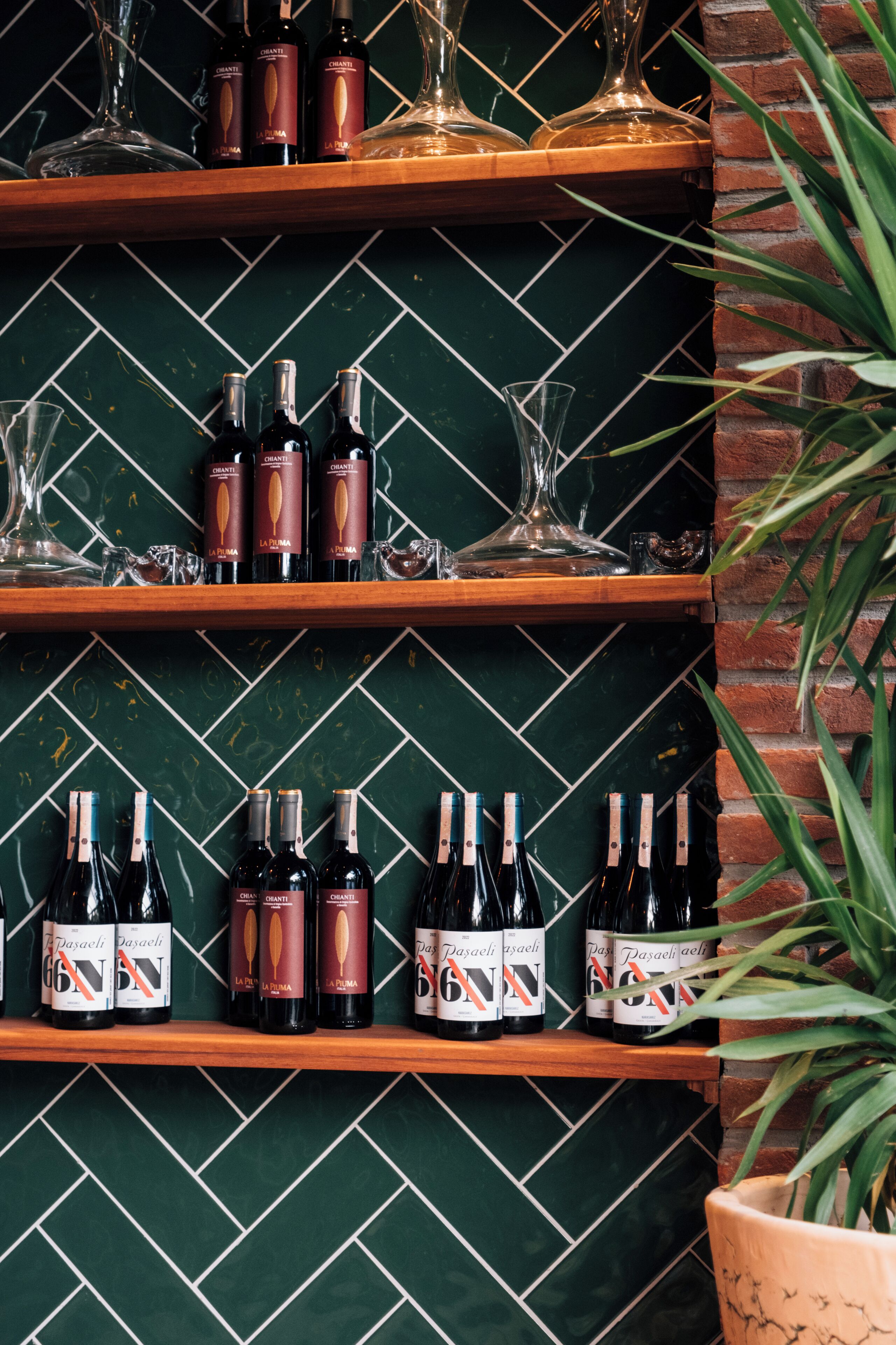 Una botellera con botellas y copas frente a una pared de azulejos verdes.