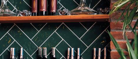 Una botellera con botellas y copas frente a una pared de azulejos verdes.