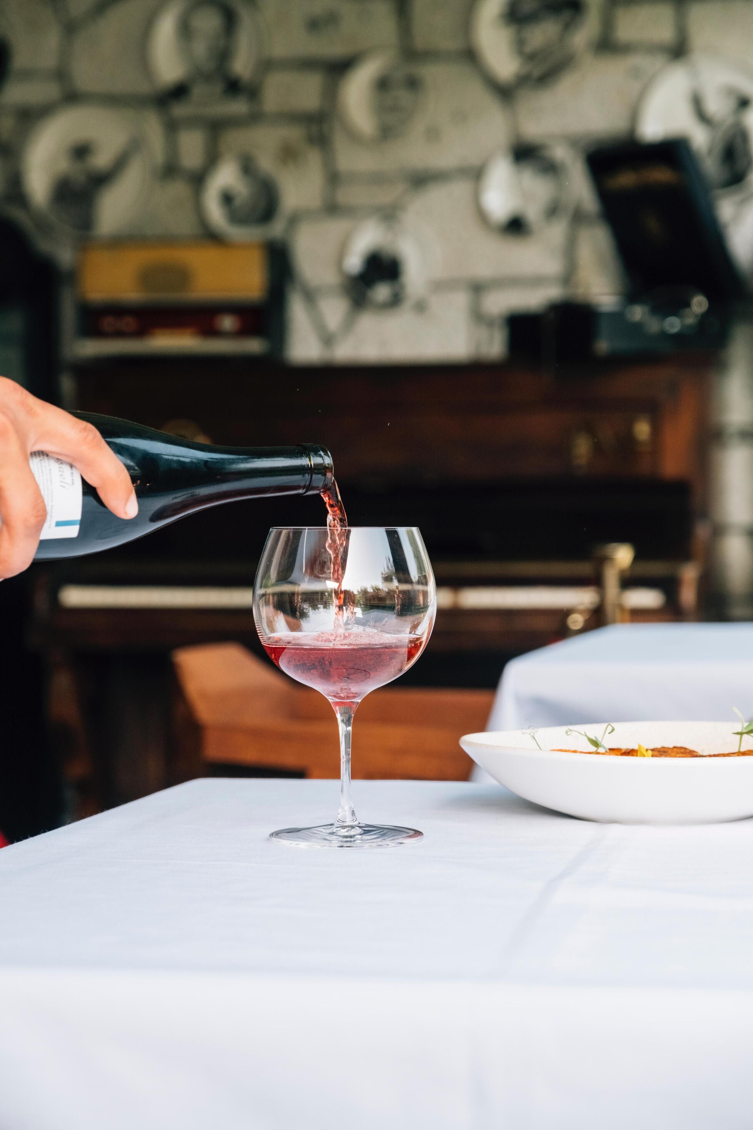 A hand pouring red wine into a glass on a table.