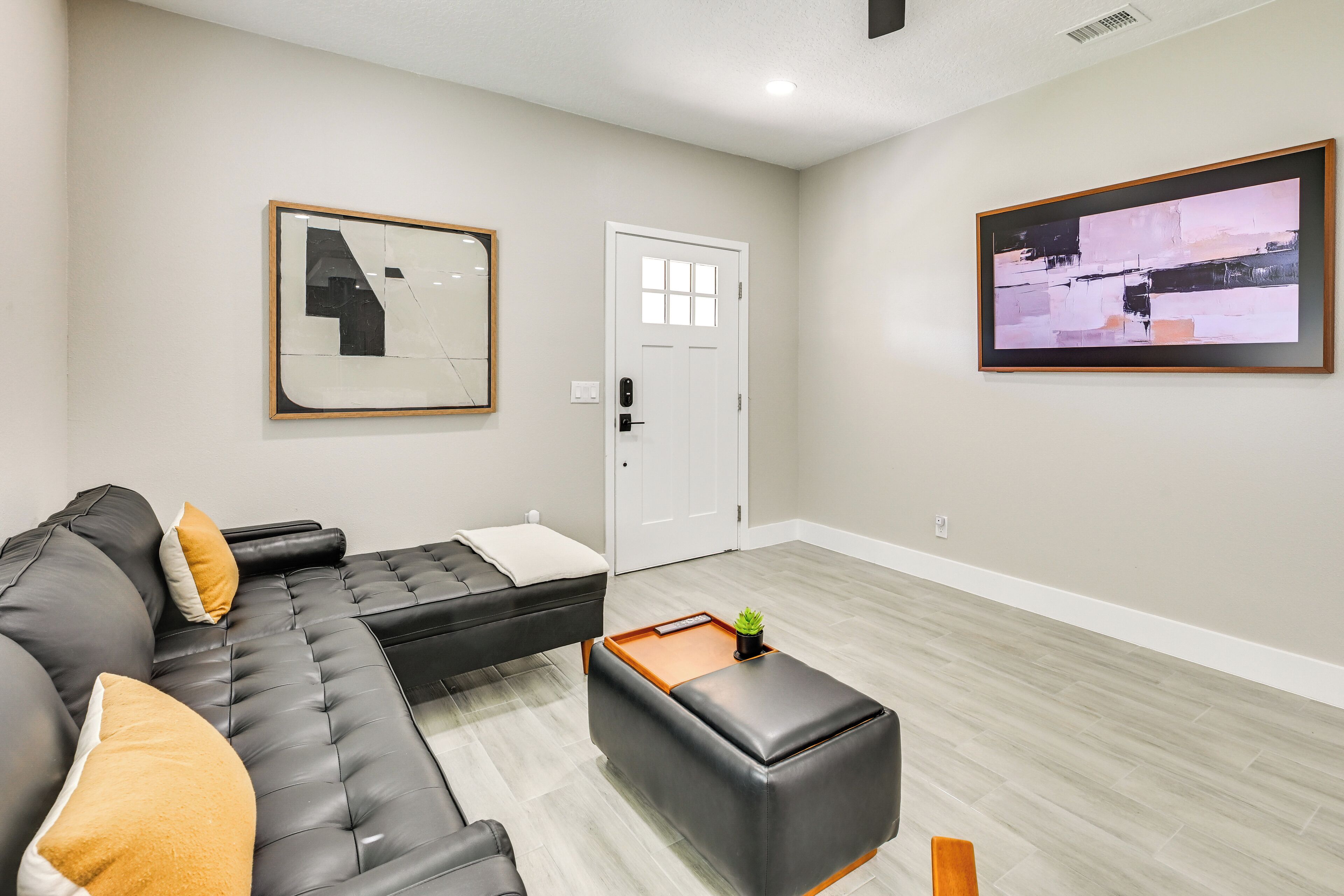 Una sala moderna con un sofá modular, un pequeño otomaní y una puerta que conduce a otra habitación.