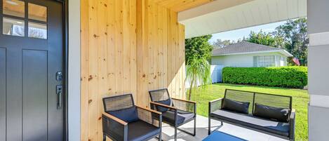 A modern outdoor seating area with a black door, wooden walls, and a view of a green lawn and house in the background.