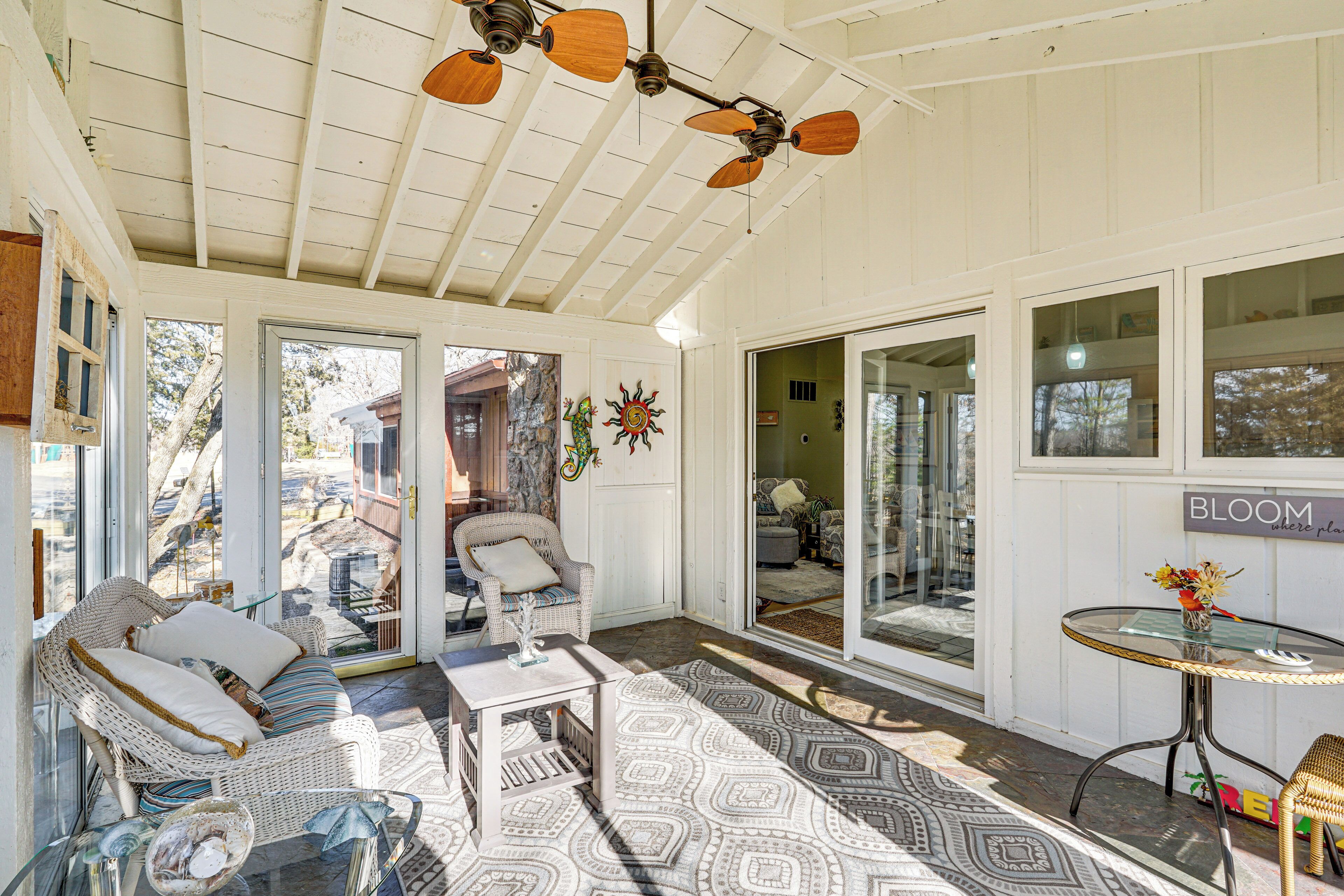 A sunlit room with a wicker sofa, a glass table, and a ceiling fan.