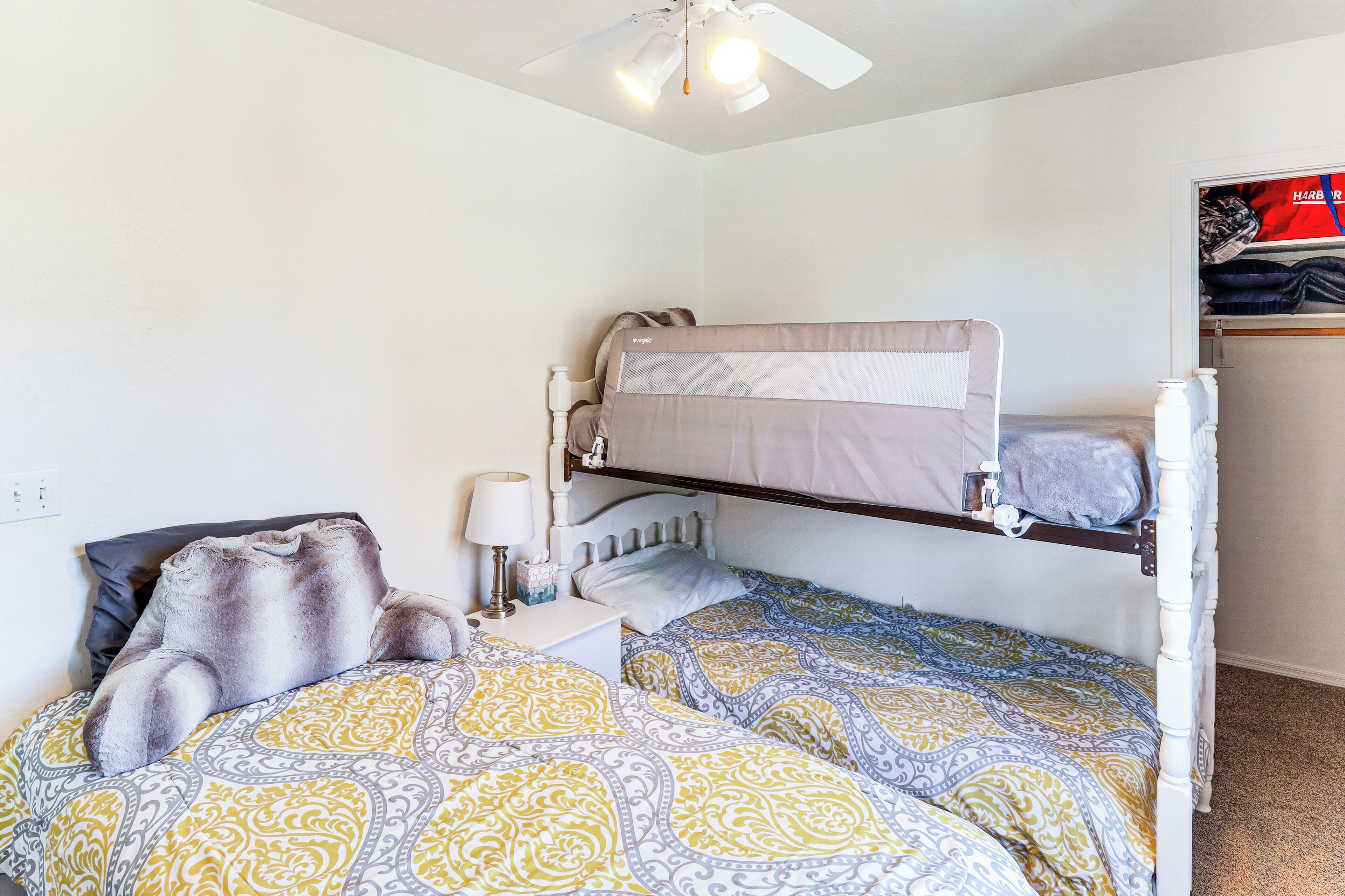 A bunk bed room with a ceiling fan, a bedside table with a lamp, and a wardrobe with a red and white design.