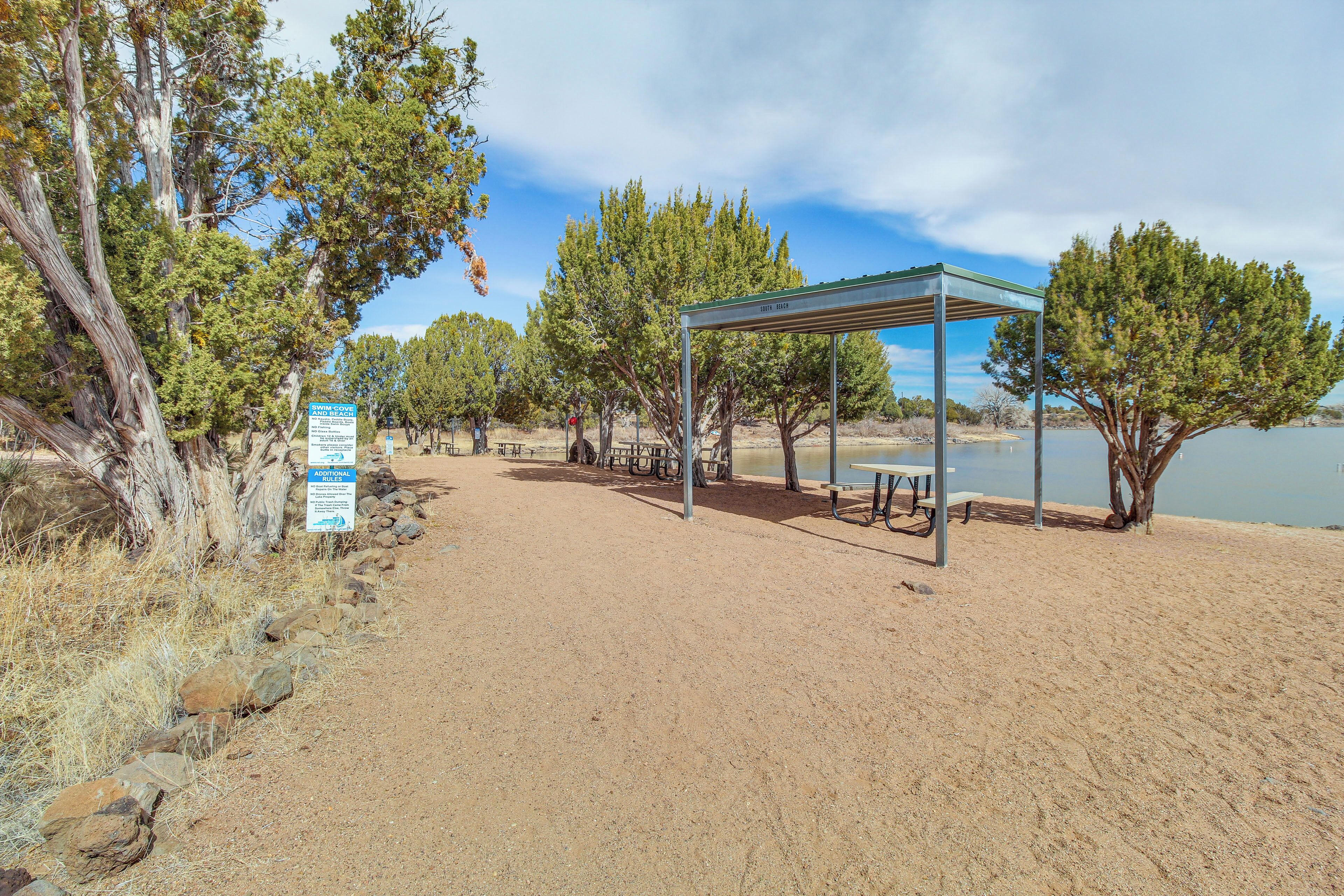 Een zandstrand met een overdekte kiosk, picknicktafels en een informatiebord.