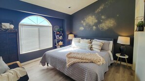 Una camera da letto con un letto grande, due lampade ai comodini, una finestra con persiane, un piccolo tavolino e una sedia.