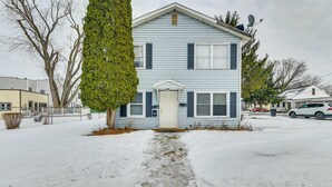 Uma casa de dois andares com uma porta da frente, um pequeno alpendre e um caminho de acesso coberto de neve.
