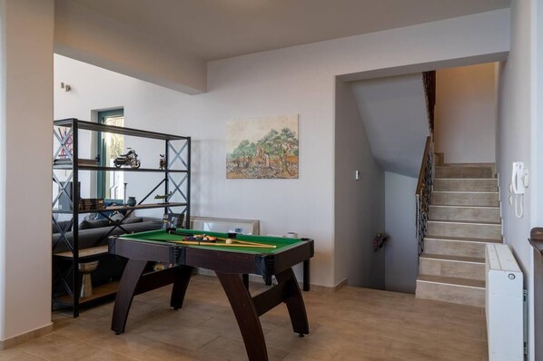 A spacious living area with a pool table, a sofa, and a bookshelf. A staircase is visible in the background.