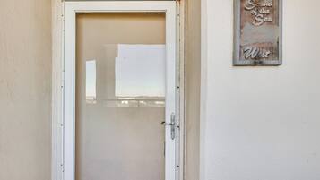 A white door with a frosted glass panel, a metal handle, and a small sign on the wall to the right that reads "Sound of the Sea West".