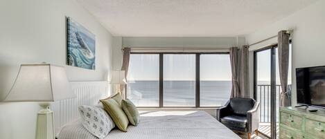 Un dormitorio con cama, una silla, televisión, cómoda y vista al océano.