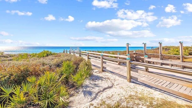 Un paseo marítimo de madera que lleva a una playa con cielos despejados y vistas al océano.