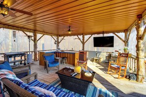 A covered outdoor seating area with wicker furniture, a bar, and a flat-screen TV.