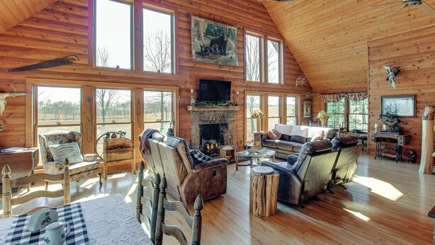A spacious wooden cabin with a fireplace, multiple seating areas, and large windows offering views of the outdoors. - Reel in Fish, Relax By Fire: Mcminnville Cabin (McMinnville)