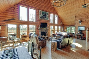 A spacious wooden cabin with a fireplace, multiple seating areas, and large windows offering views of the outdoors.