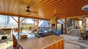 A covered outdoor area with a wooden deck, a stone fireplace, and a seating area with chairs and a table. - Reel in Fish, Relax By Fire: Mcminnville Cabin (McMinnville)