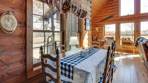 A wooden cabin interior with a checkered tablecloth, wooden chairs, a lamp, and a large window. - Reel in Fish, Relax By Fire: Mcminnville Cabin (McMinnville)