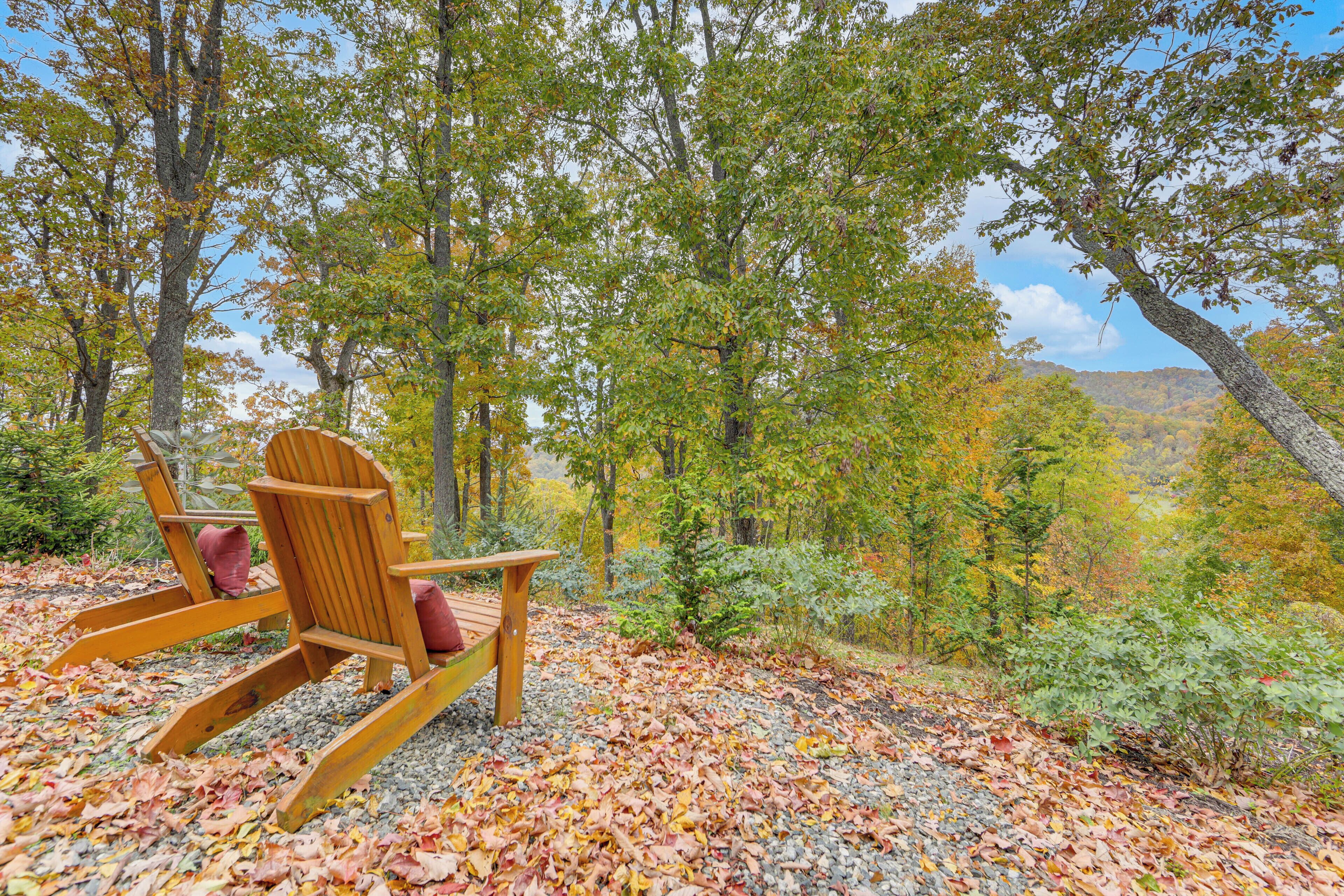 Ein hölzerner Adirondack-Stuhl mit Kissen auf einem Kiesweg, umgeben von Herbstlaub.