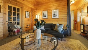 A cozy log cabin interior with a wooden floor, a glass coffee table, a sofa, and a fireplace. - Secluded Mtn-view Retreat in Mars Hill (Mars Hill)