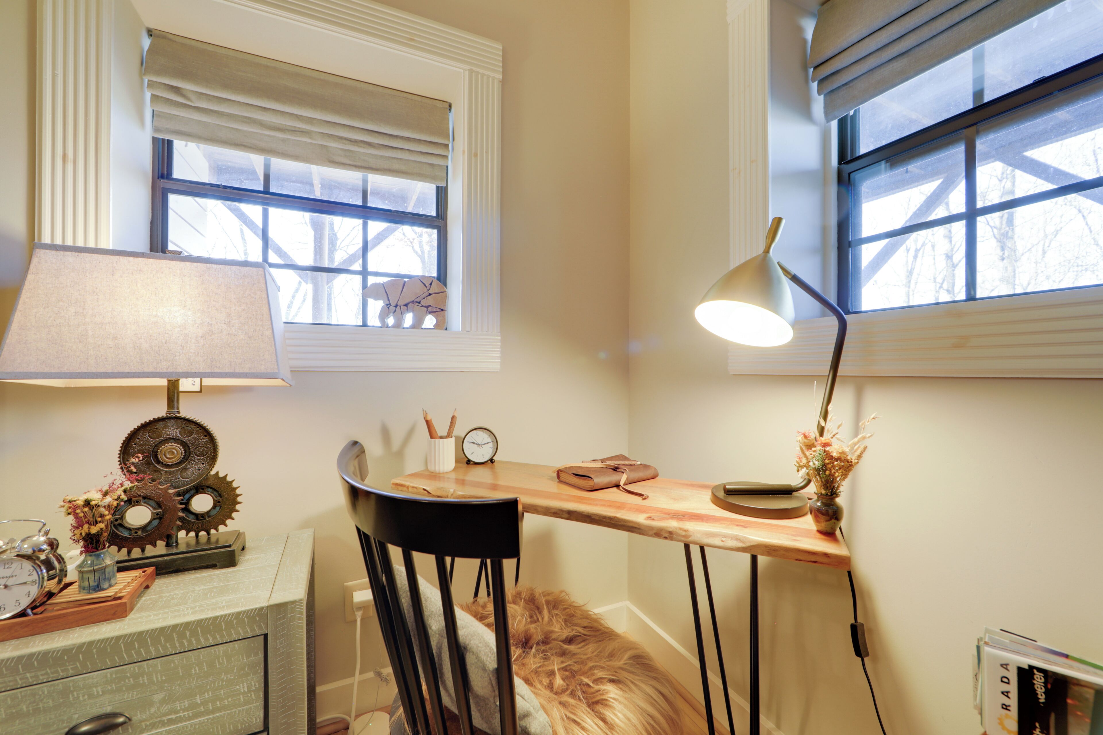 Ein Zimmer mit Schreibtisch, Stuhl, Lampe, einer Uhr und Dekorationselementen.