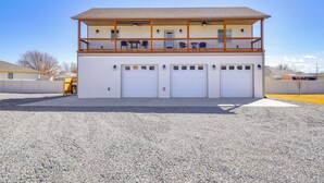 Um edifício de dois andares com varanda, várias garagens e entrada por caminho de cascalho.