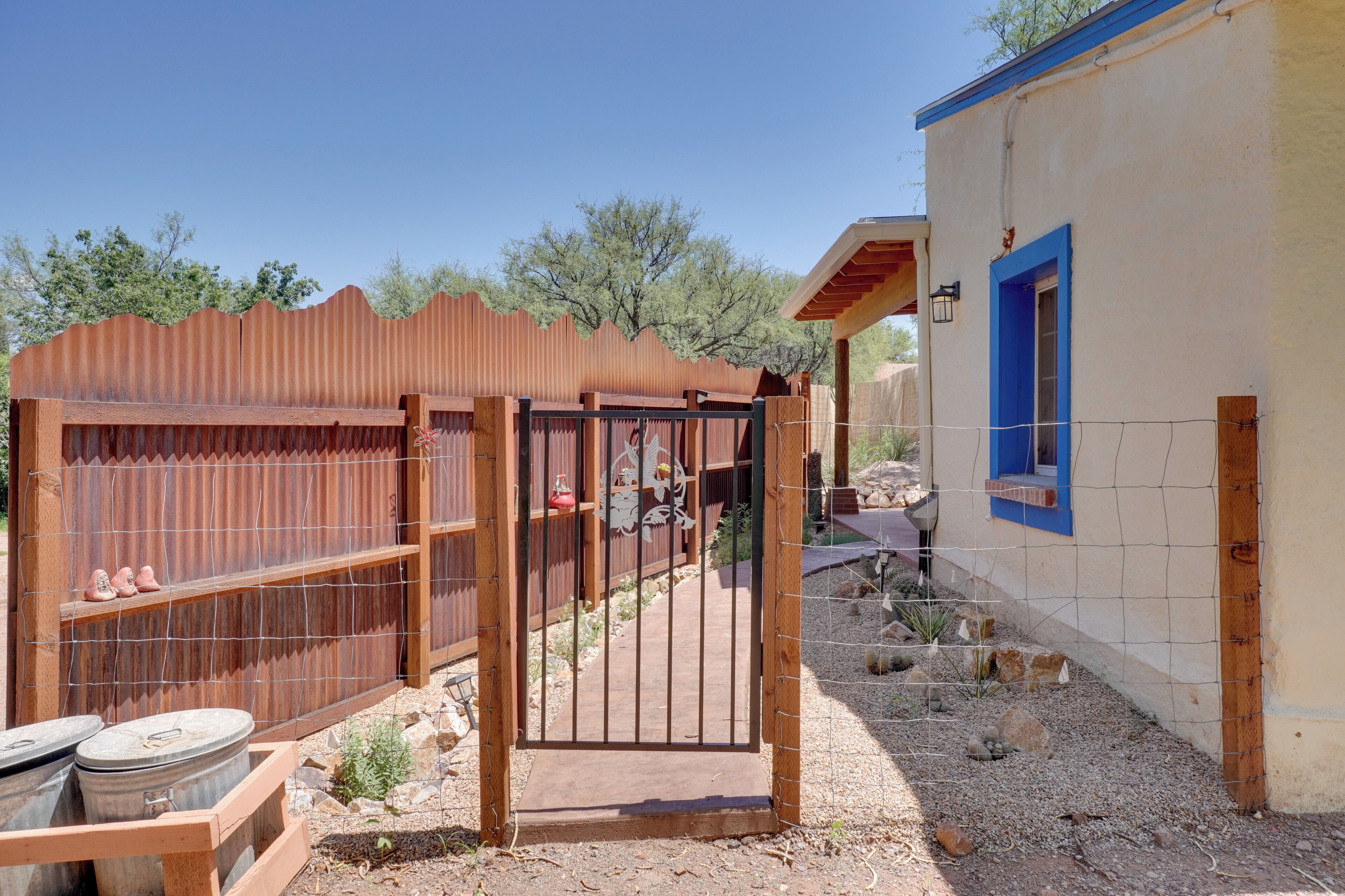 A fenced outdoor area with a gate, a small shed, and a building with a blue window.