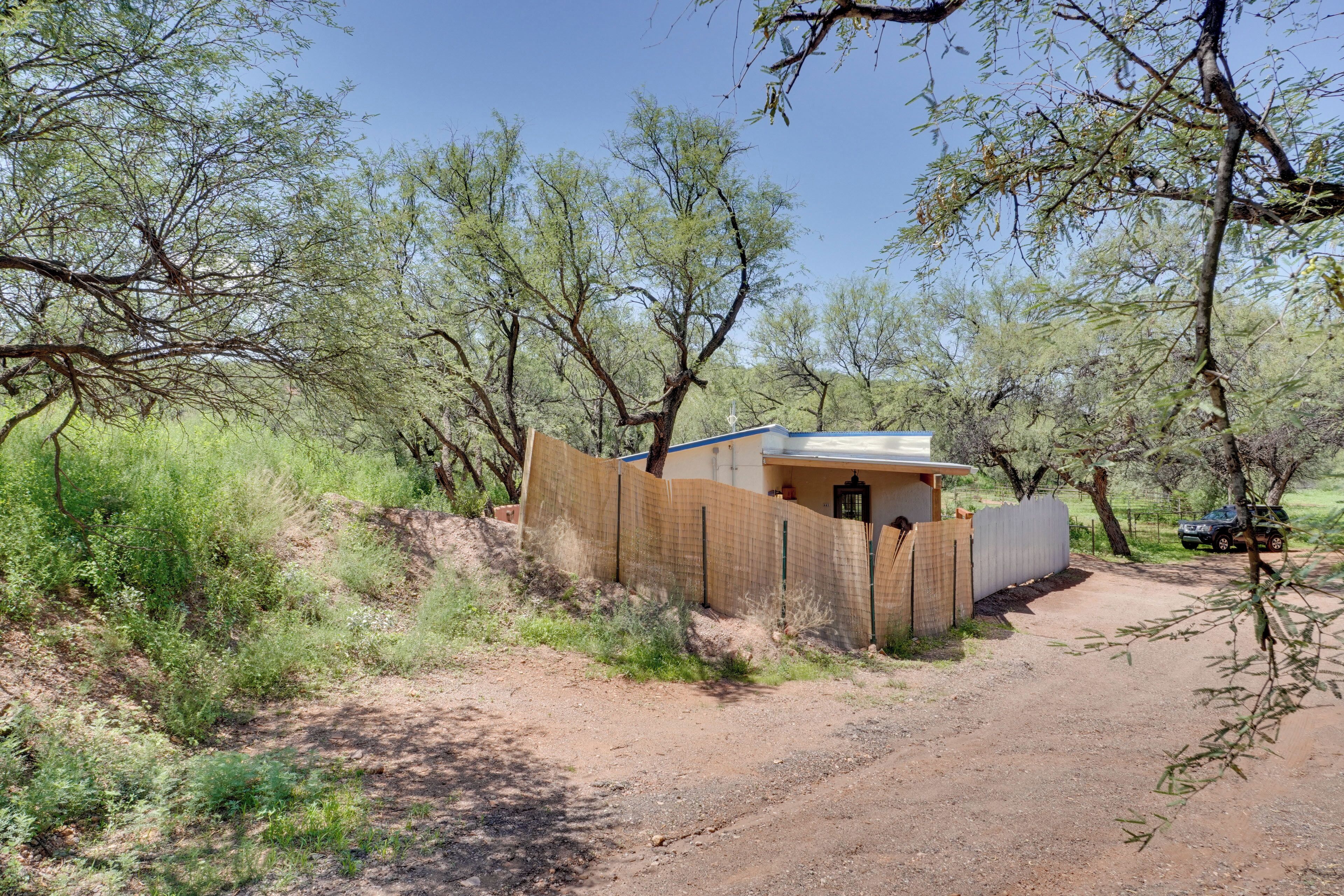 A small building with a fenced entrance, surrounded by trees and a dirt path.