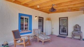A covered patio area with wooden furniture, a rocking chair, a small table, and a refrigerator.