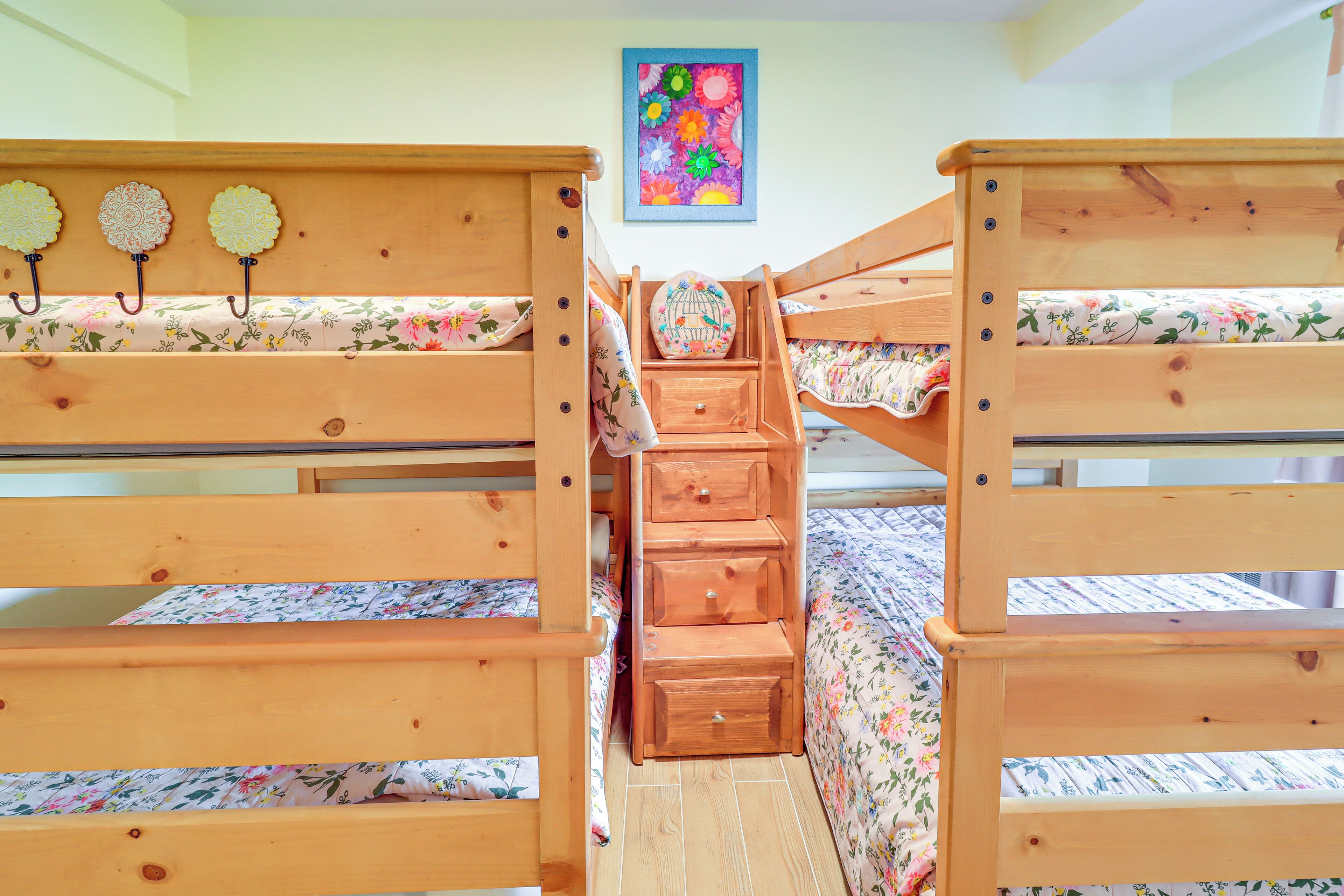 A bunk bed room with a wooden ladder, floral bedding, and a colorful wall decoration.