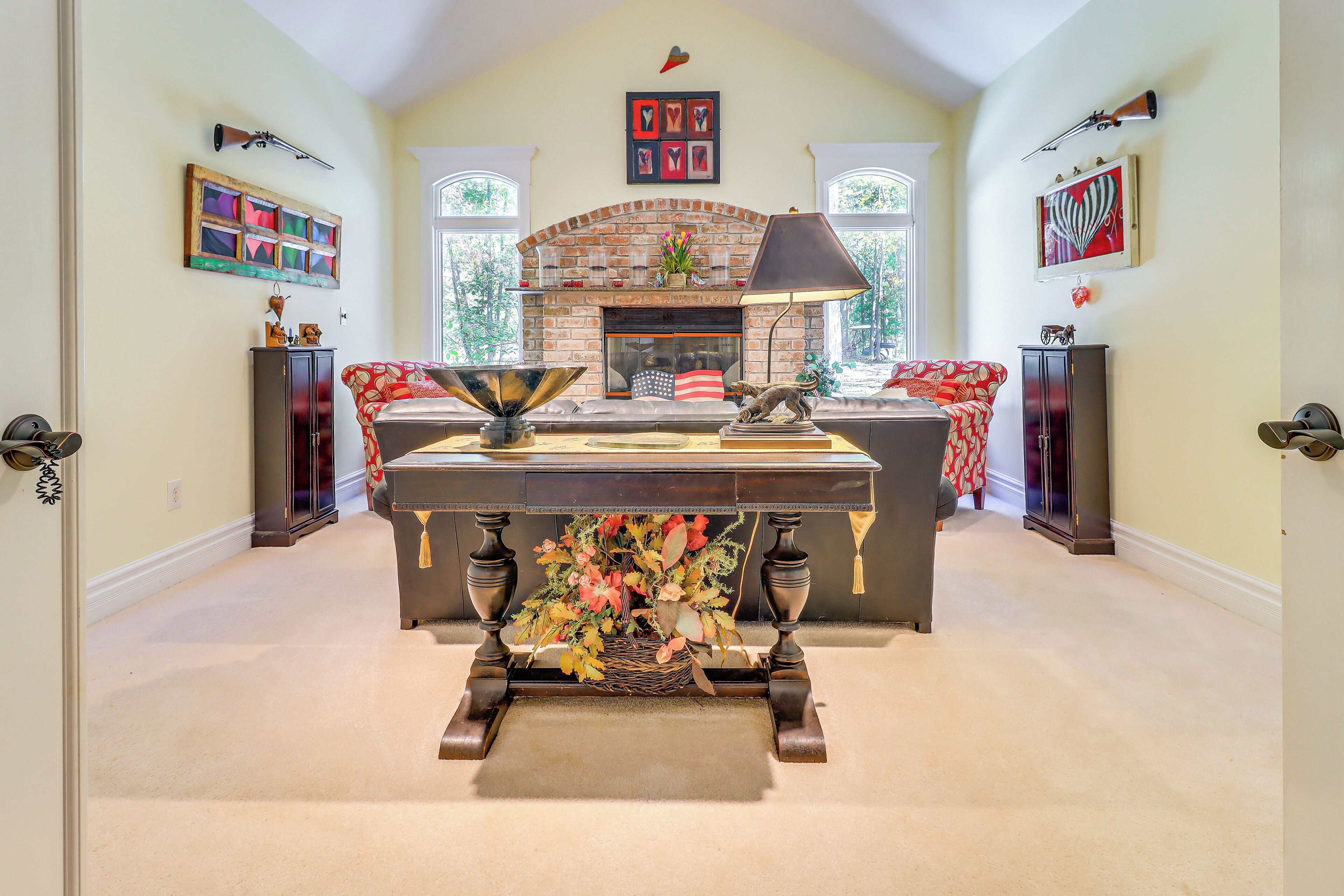 A dining area with a brick fireplace, a table with a floral centerpiece, and a view of the outdoors through large windows.