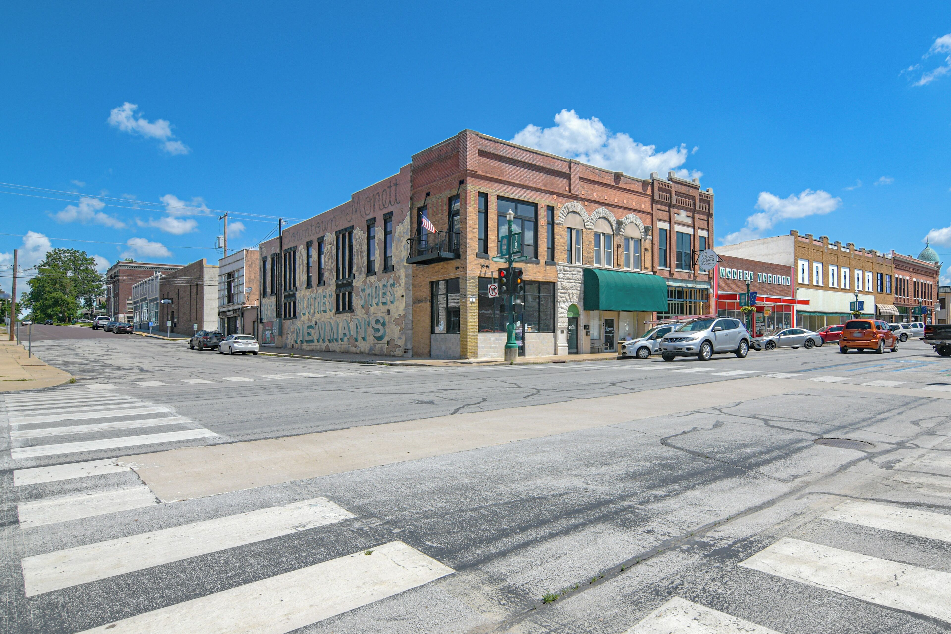 A street view with buildings, a crosswalk, and parked cars.