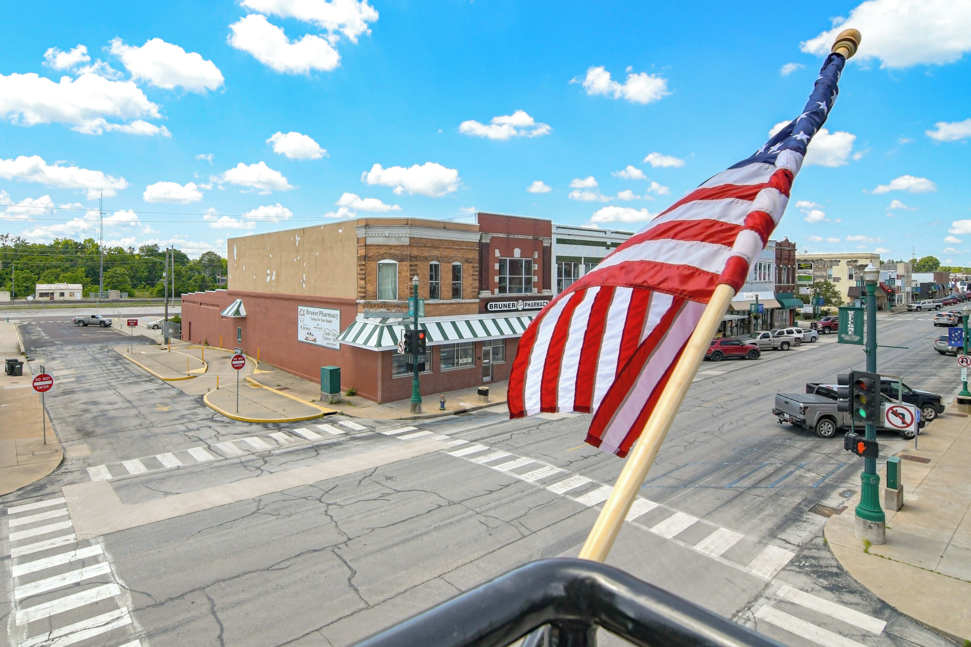 A street view with a flagpole displaying an American flag, a pharmacy, and a crosswalk.