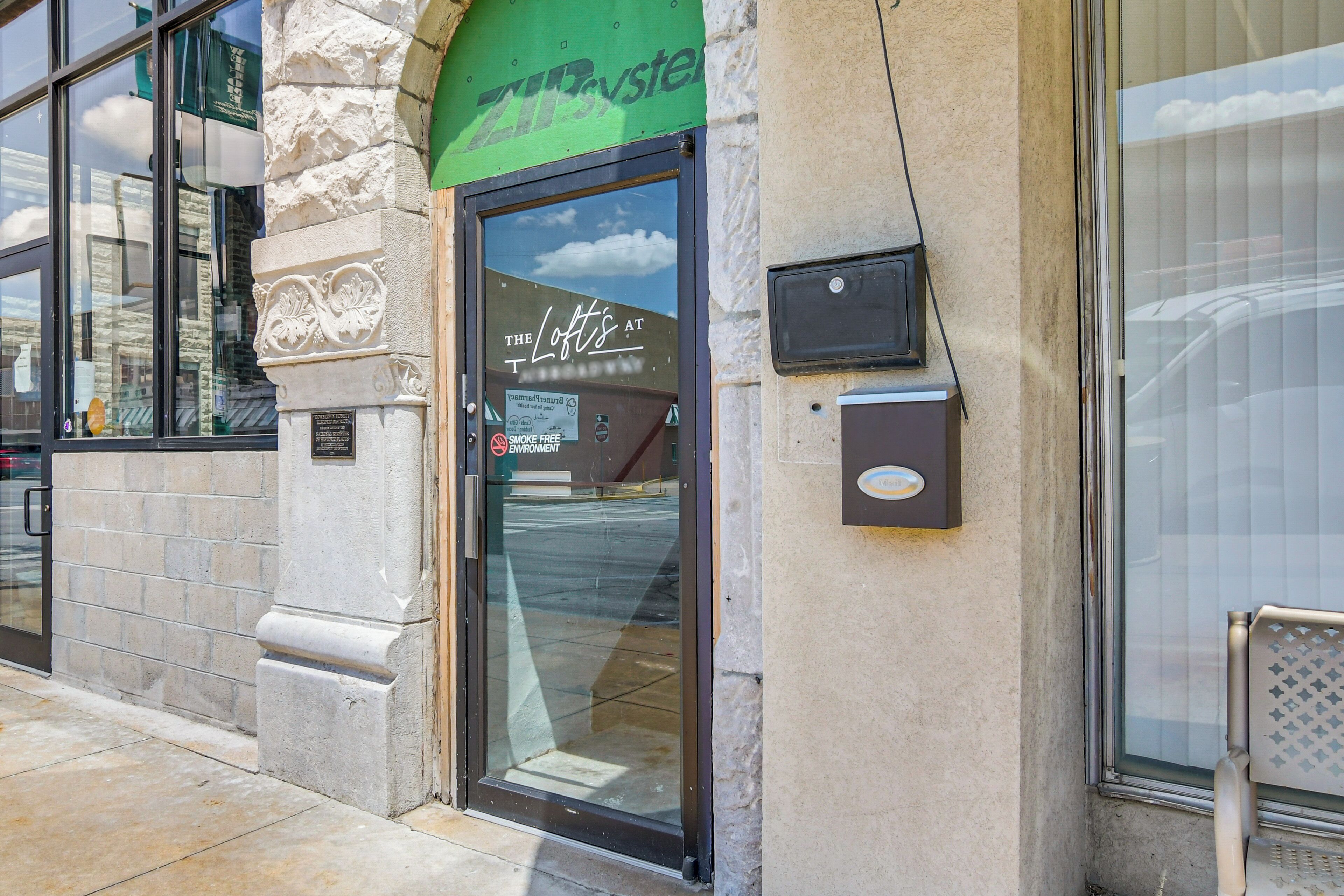 A building entrance with a stone facade, a green awning, and a glass door with a sign reading "The Loft's at".