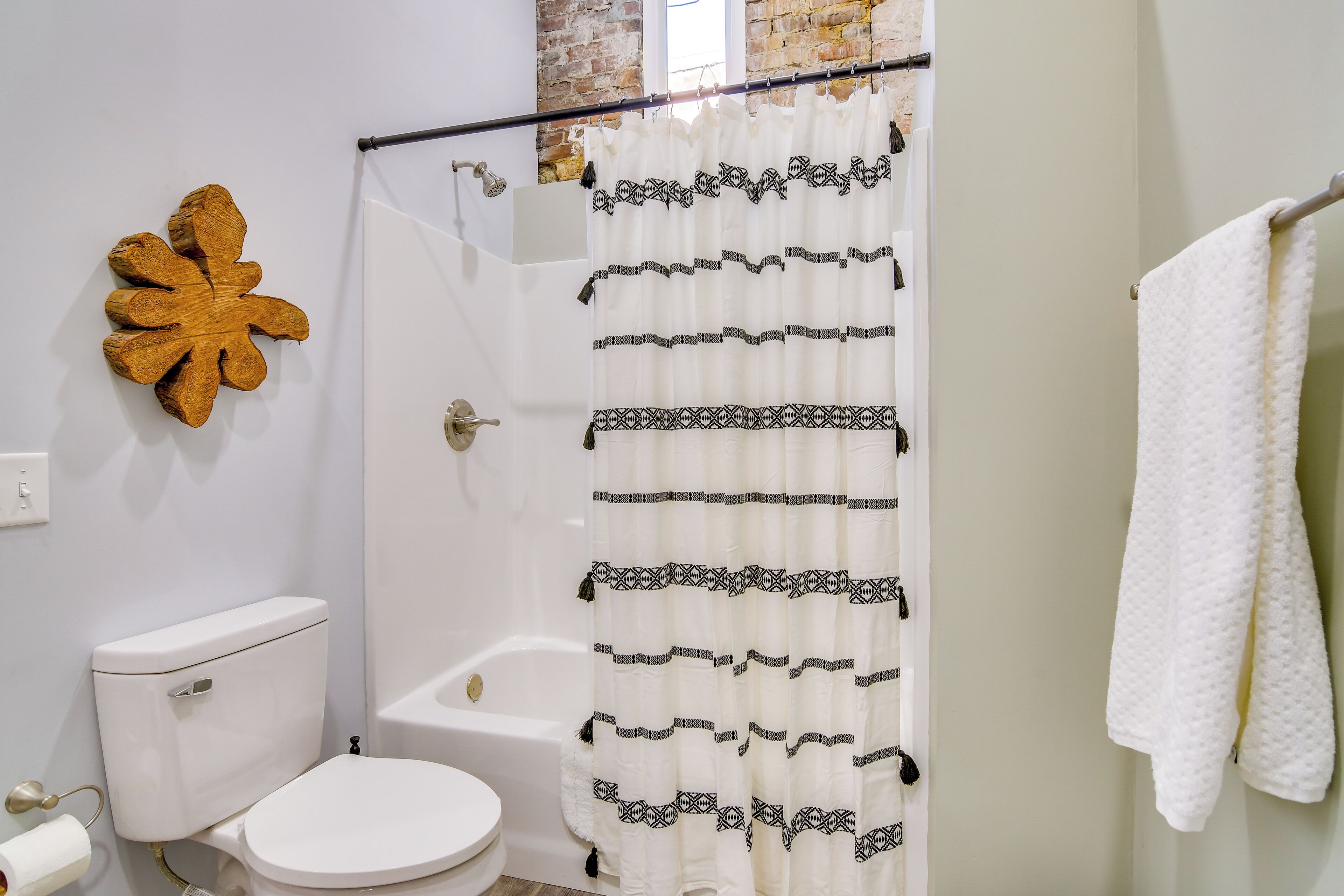Une salle de bain avec des toilettes blanches, une baignoire blanche, un rideau de douche à motifs noirs, une serviette blanche posée sur un porte-serviettes et une décoration murale en bois.