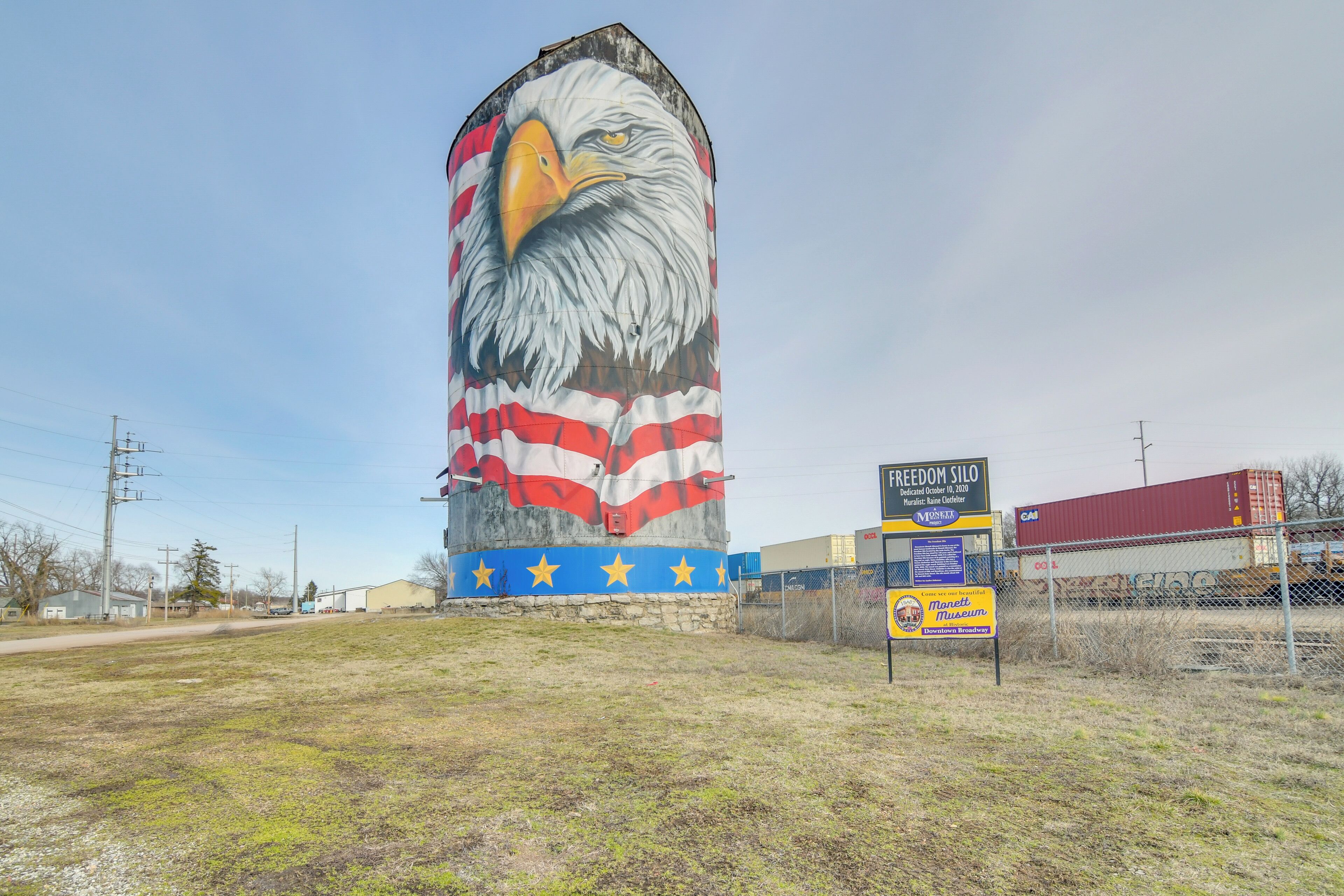 A large mural of an eagle with an American flag design at its base, located in an open field with a sign for the Freedom Silo nearby.