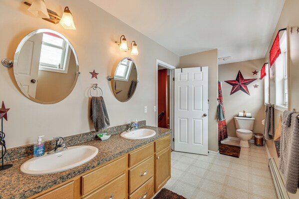 A bathroom with two sinks, a large mirror, and a door leading to another room. - The Gathering Place: Rushville Home w/ Hot Tub (Rushville)