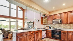 A spacious kitchen with wooden cabinets, a large island, and a view of the outdoors. - The Gathering Place: Rushville Home w/ Hot Tub (Rushville)